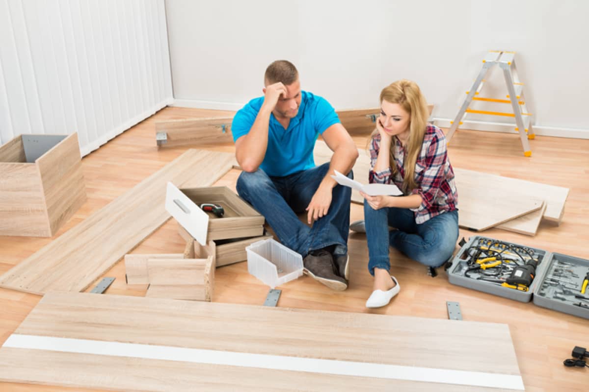 A strait presenting couple disassemble furniture on the ground.
