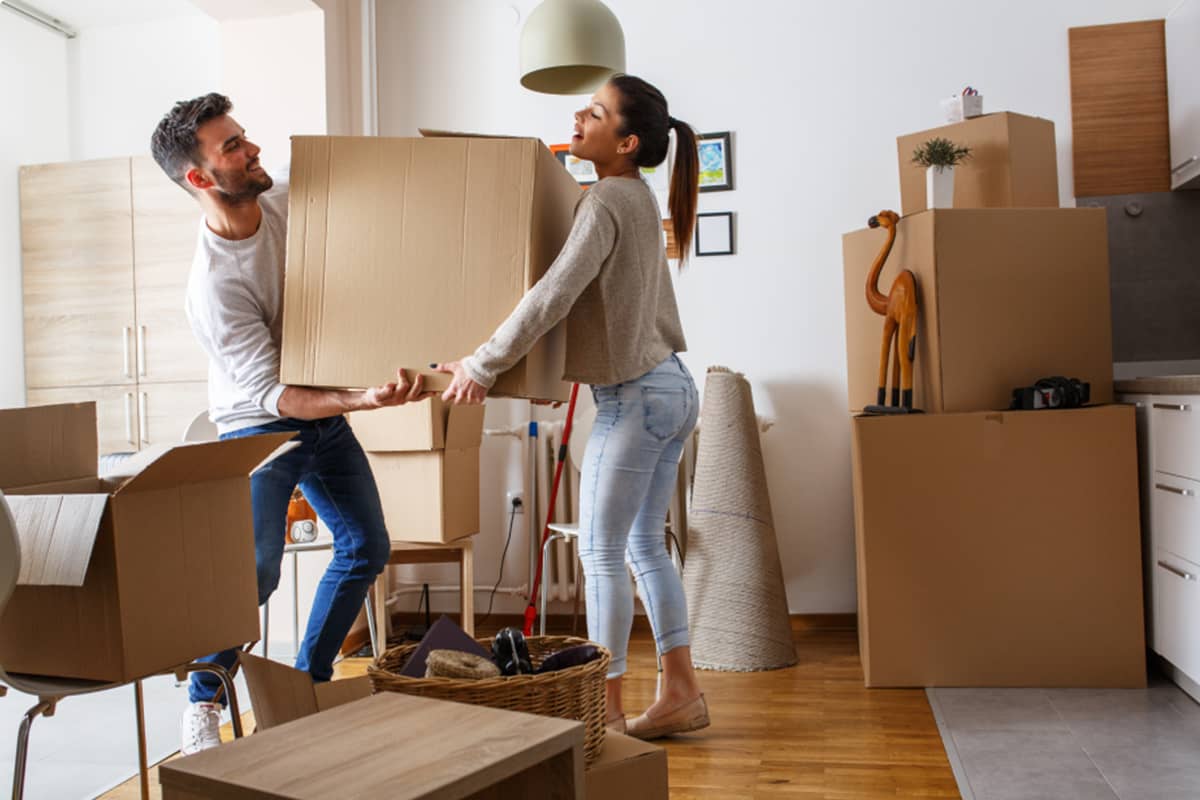 A strait-presenting couple is moving boxes in a room in a house.