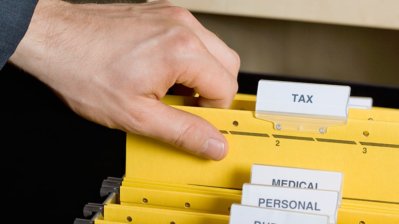 A hand sorts through tax files in a drawer